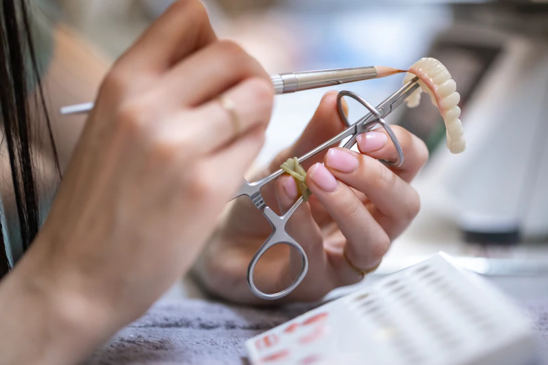 Hands shaping a set of false teeth with fine tools
