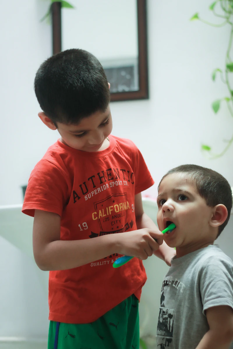 An older boy helping his little brother brush his teeth at the bathroom sink