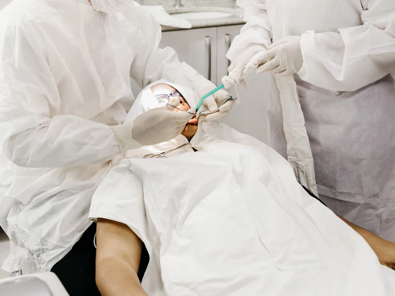 Two dentists in gowns and gloves working on a patient in the dental chair